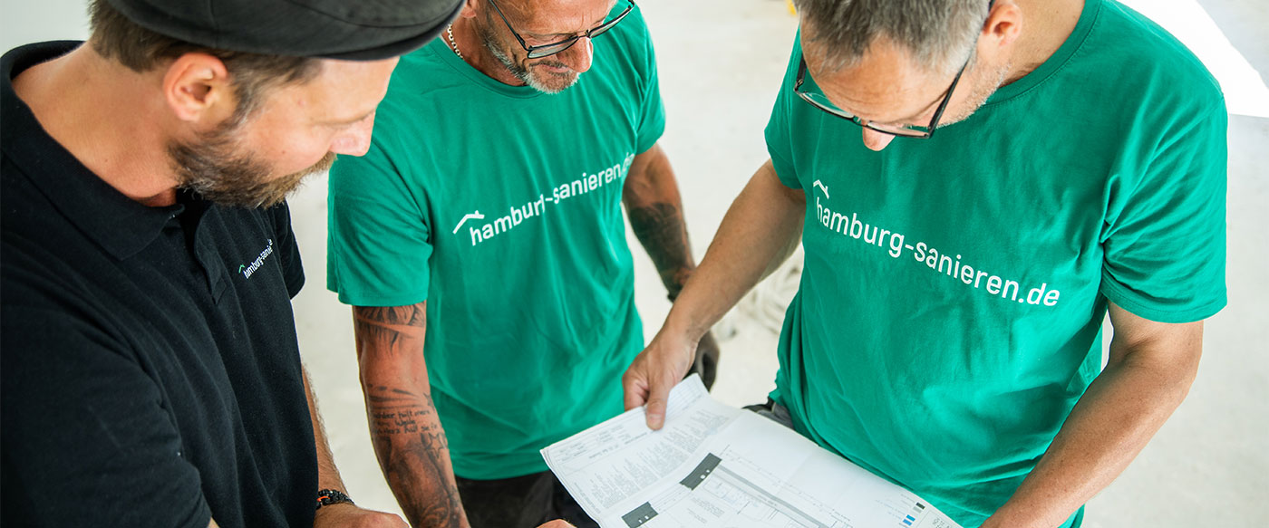 Drei Bauprofis von hamburg-sanieren.de besprechen Baupläne auf einer Baustelle, mit Fokus auf professionelle Sanierungsplanung.