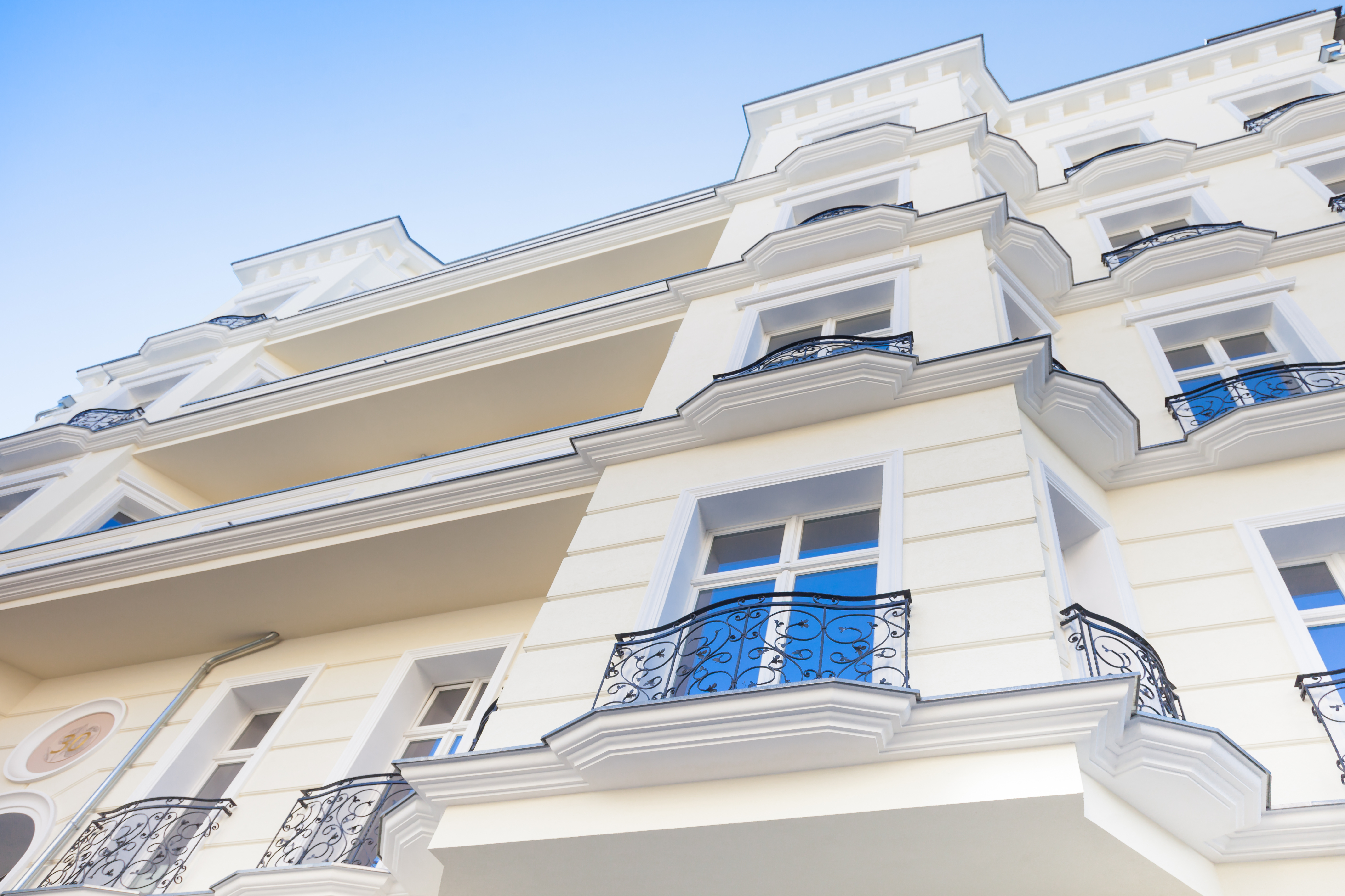 Fassade eines sanierten Mehrfamilienhauses mit dekorativen Balkonen und weißem Anstrich, im klassischen Architekturstil unter blauem Himmel.